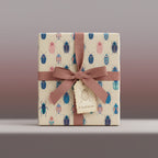 Square gift wrapped in cute beetle-print paper, tied with a mauve ribbon and a gift tag.
