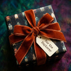 Unique gift wrap with vintage beetle print, tied with a rust-colored velvet ribbon and "For the Explorer" tag.
