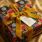 Elegant square gift wrapped in vintage floral wrapping paper with gold velvet ribbon and "A Little Something" tag.
