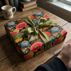 Gift wrapped in colorful floral wrapping paper with green ribbon on rustic wood table.