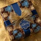 Elegant floral wrapping paper in blue and gold with a gold mesh bow and "Cheers" tag.