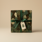 Square gift wrapped in forest green Christmas wrapping paper with pinecone pattern and satin ribbon.