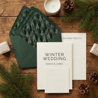 Rustic winter wedding invitation with pine tree envelope liners by Wrapped Studios on a wooden table.