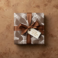 Square gift wrapped in brown leaf pattern paper with brown satin ribbon and "A Little Something For You" tag.
