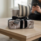 Elegant leaf-patterned gift wrapped in brown and white paper with black velvet ribbon.