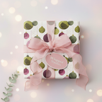Christmas gift wrap with modern ornaments in olive green and deep pink, tied with a sheer pink ribbon and tag, on a soft bokeh background.
