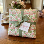 Elegant pink and green floral wrapping paper with a sage ribbon and tag by Wrapped Studios.