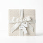 Elegant beige First Communion wrapping paper with a white velvet bow and cross tag by Wrapped Studios.