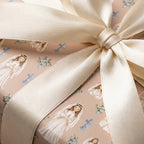 First Communion wrapping paper with praying girls and blue crosses, tied with a cream satin bow by Wrapped Studios.