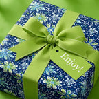 Dark blue floral wrapping paper with a lime ribbon and tag saying "Enjoy!" Wrapped Studios.