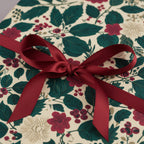 Elegant Christmas gift wrap with a burgundy bow and floral, berry, and leaf pattern.