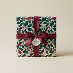 Elegant gift wrapped in botanical floral wrapping paper with a burgundy ribbon and “a thoughtful gesture” tag.