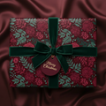 Burgundy floral Christmas gift wrap with velvet ribbon and "Merry Christmas" tag on a silk background.