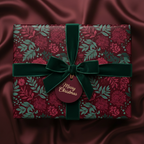 Burgundy floral Christmas gift wrap with velvet ribbon and "Merry Christmas" tag on a silk background.