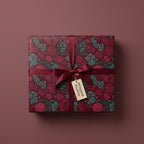 Burgundy floral wrapping paper on a square gift box, tied with a matching satin ribbon and tag.