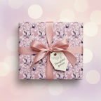Gift box wrapped in elegant lilac floral wrapping paper with a pink satin ribbon and "Thoughtful Gesture" tag.