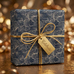 Elegant navy blue gift wrapped in abstract floral wrapping paper with gold ribbon, tag says "Celebrate."