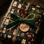 Cute cat Christmas wrapping paper by Wrapped Studios on a gift box with a green velvet bow and wooden Noel tag.