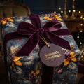 Elegant Christmas gift wrap with pinecone floral pattern, velvet bow, and "Season's Greetings" tag.