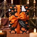 Spooky Halloween wrapping paper with pumpkins and black cats, tied with an orange satin bow by Wrapped Studios.