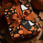 Spooky Halloween wrapping paper with cats and ghosts, tied with an orange ribbon by Wrapped Studios.