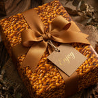 Gift box wrapped in modern brown pattern paper with a gold ribbon bow and "Enjoy" tag.