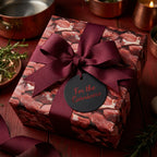 Square gift wrapped in meat print wrapping paper with a wine-colored ribbon and "For the Carnivore" tag.