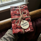 Rectangular gift wrapped in funny raw meat patterned wrapping paper with twine bow and a "Wrapped Studios" tag.