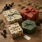 Rustic alligator print wrapping paper (tan/dark green) with string, solid green/terracotta gifts on wood. Wrapped Studios.
