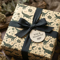 Beige alligator & botanical wrapping paper with dark green ribbon and "Wild & Wonderful" tag. Rustic nature-themed gift wrap.