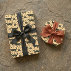 Tan alligator & botanical print wrapping paper with dark green details, tied with black and rust ribbons. Unique nature gift wrap.