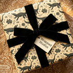 Beige alligator print wrapping paper with black botanical details, black velvet bow, and Wrapped Studios gift tag.