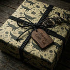 Khaki alligator & floral wrapping paper with black twine and a rustic wood gift tag on a dark table.