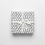 Modern black and white pebble pattern wrapping paper with a white ribbon and "Wrapped Studios" gift tag, perfect for any occasion.