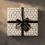 Luxury white and gold abstract pattern wrapping paper with a black ribbon bow and "Elegant Gesture" gift tag on a stone background.