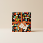 Modern gift box wrapped in geometric wrapping paper with orange ribbon and "Wrapped Studios" tag.