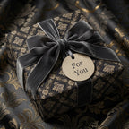 Luxury black and gold damask wrapping paper with a grey velvet bow and tag by Wrapped Studios.