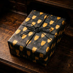 Luxury champagne gift wrap with gold glasses on black box with twine and wax seal by Wrapped Studios.