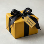 Elegant gold wrapping paper with black satin ribbon on a square gift box, ideal for birthdays or special occasions.