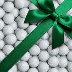 Golf wrapping paper featuring a white golf ball pattern with a green satin ribbon bow by Wrapped Studios.