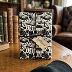 Gothic wrapping paper with spellbook and skull patterns by Wrapped Studios, tied with black twine on a wooden table.