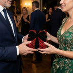 Man hands woman a gift in luxury gothic red and black wrapping paper with velvet bow by Wrapped Studios.