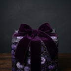 Gothic wrapping paper with purple floral and pumpkin patterns, tied with a velvet bow by Wrapped Studios.