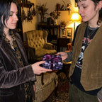 Friends exchanging a gift in gothic mushroom wrapping paper with purple ribbon, by Wrapped Studios.