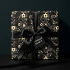 Luxury black floral wrapping paper with vintage birds and cream flowers, tied with a black satin bow. Wrapped Studios.