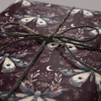 Burgundy gift box wrapped in moth and moon patterned paper, tied with a gray twine bow.