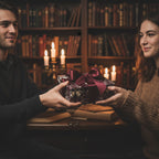 Woman receiving gift wrapped in luxury floral wrapping paper with burgundy ribbon in cozy library setting.