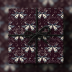 Elegant gift box wrapped in dark floral wrapping paper with moth and moon pattern, tied with a black cord bow.