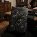Gothic raven wrapping paper with a black twine bow, dark aesthetic gift wrap by Wrapped Studios.