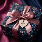 Luxury gift wrapped in moody floral and raven print paper with a pink satin bow and "With love" tag by Wrapped Studios.